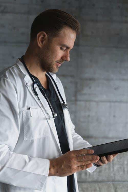 A doctor holding a black tablet computer, reviewing patient health data and prescription history.