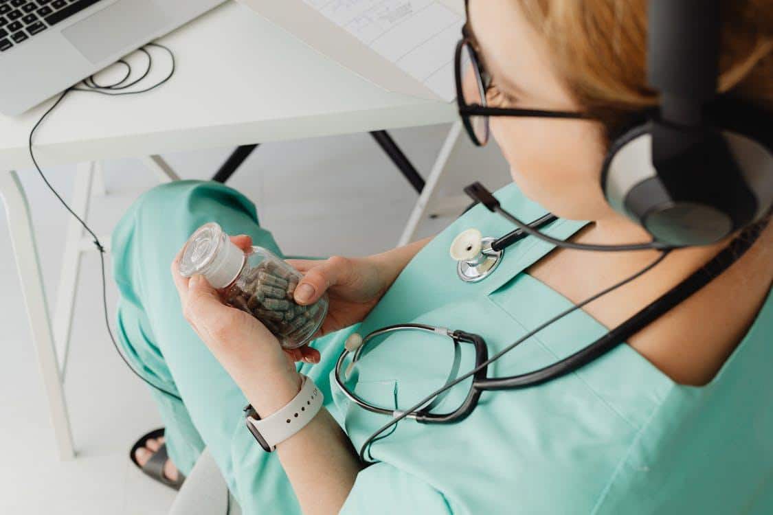 Doctor holding a bottle of pills while consulting a patient remotely using a laptop.