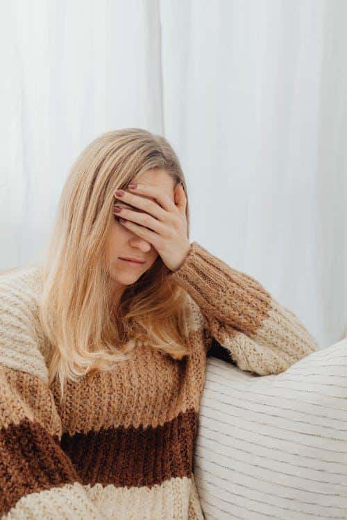 A person sitting with their eyes closed and a hand pressed against their forehead, appearing anxious and overwhelmed.