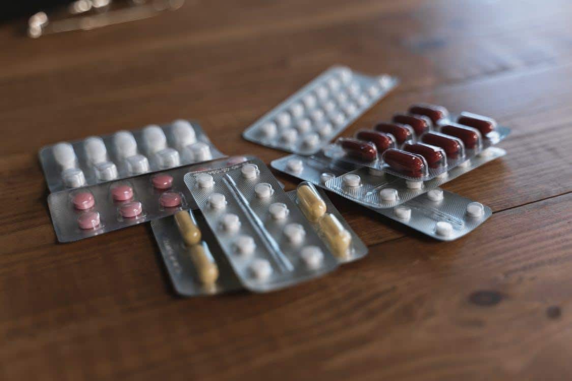 Several blister packs of various tablets scattered on a wooden surface.