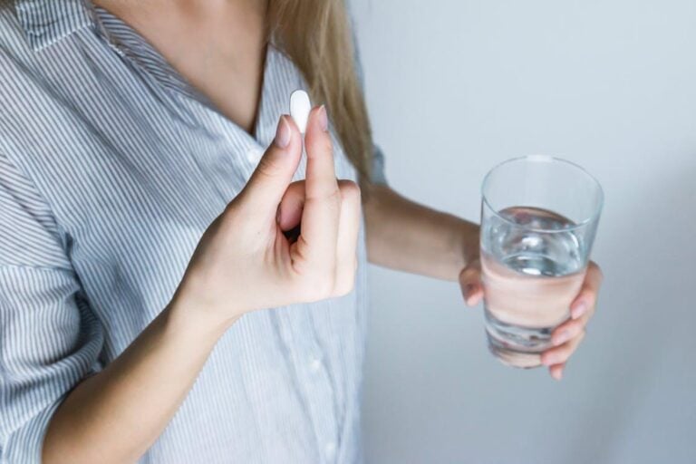 Woman holding a half-full glass of water and a white pill, preparing to take her prescribed medication.