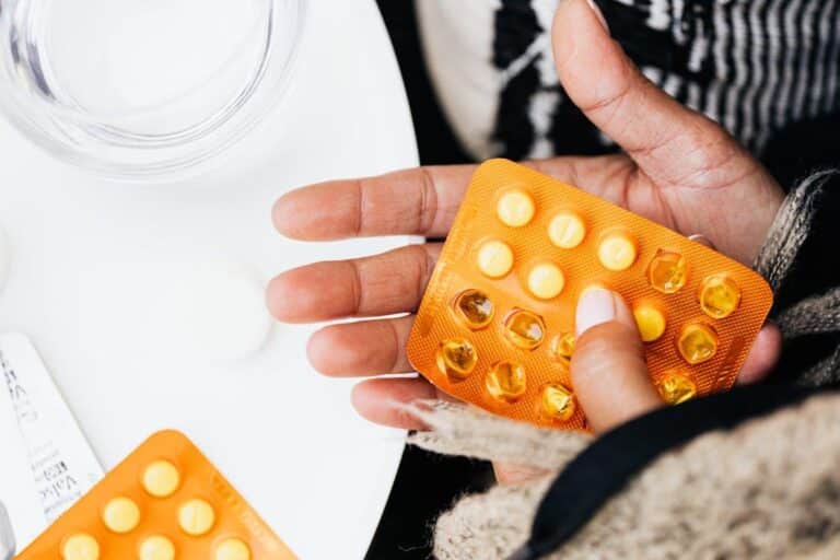 Person holding a yellow blister pack of pills in their hand, illustrating daily medication management.