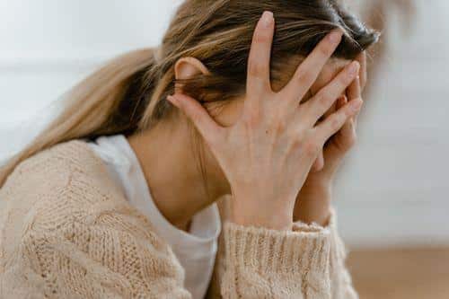 Woman sitting with face covered by hands showing signs of depression