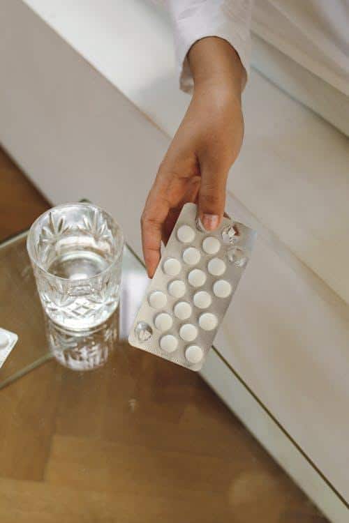 Woman picking up medication from a blister pack to take a prescribed dose.